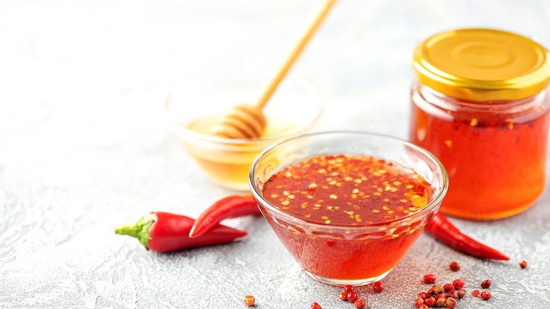 A small glass bowl of hot honey sits next to a jar of hot honey with a gold lid