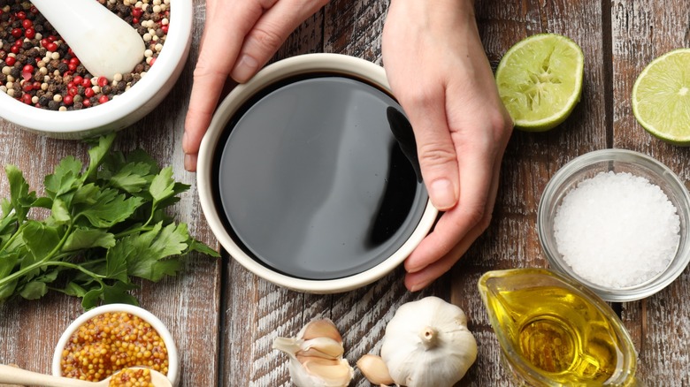 hands holding a bowl of soy sauce with olive oil, spices, lemon, garlic, and herbs on the side