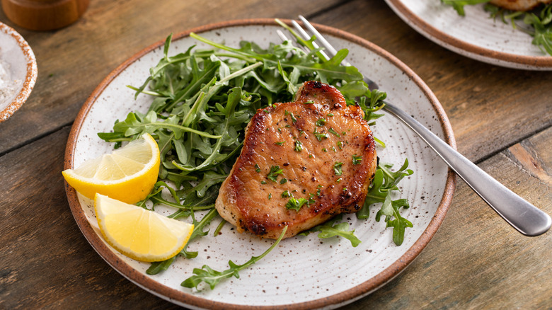Pork chop with lemon slices and an arugula salad on a plate