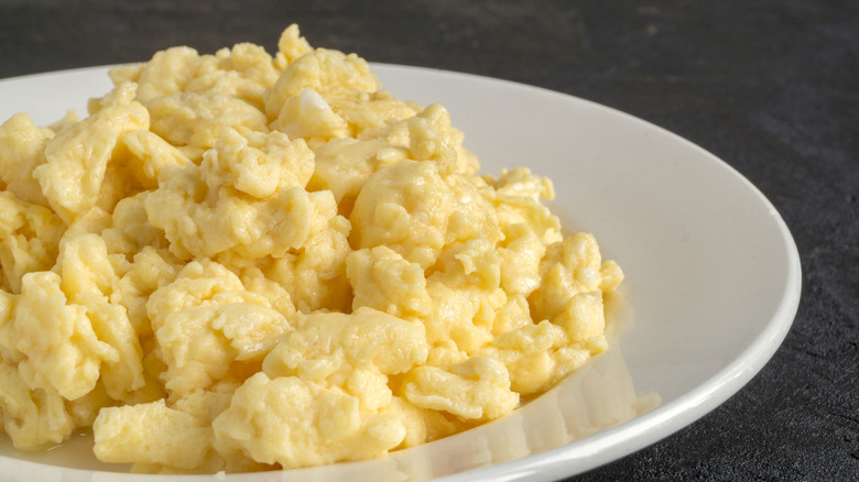 A white plate of fluffy scrambled eggs is photographed in close-up.