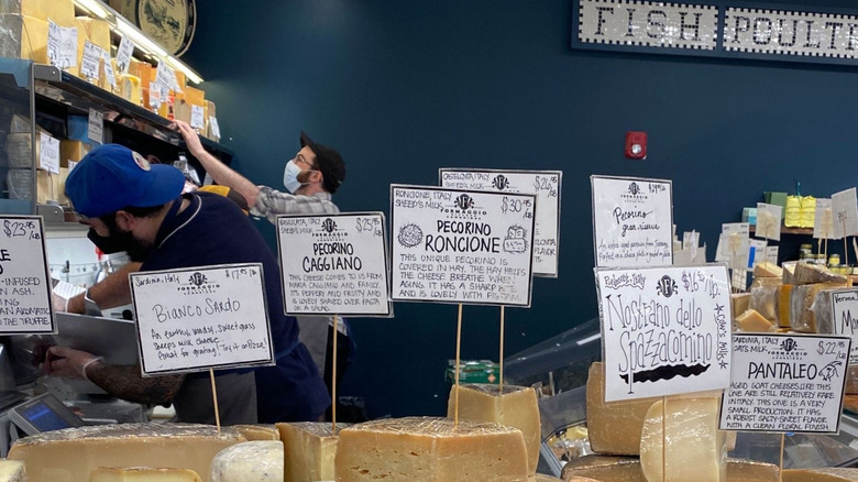 Two men slicing cheese behind a cheese counter