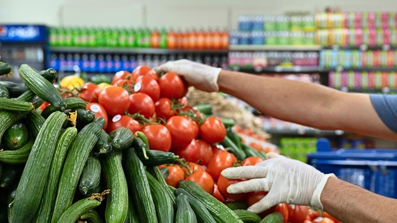 Gloved hands stocking produce in grocery store