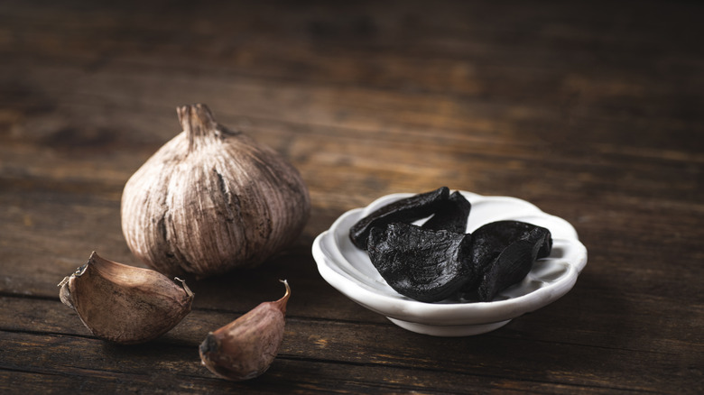 Black garlic cloves in white dish on wooden surface