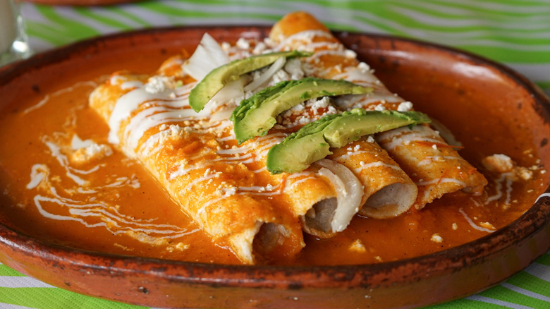 Red enchiladas with fresh avocado on a clay plate