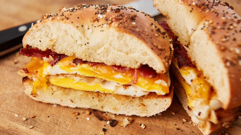 A bacon, egg, and cheese on a bagel is sliced in half on a cutting board.