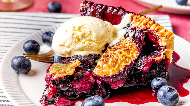 A slice of blueberry pie topped with vanilla ice cream