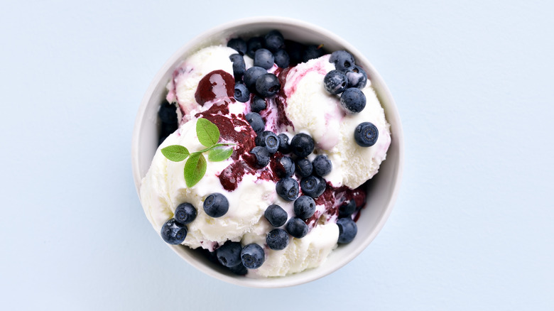 A bowl of vanilla ice cream topped with blueberry syrup and fresh blueberries