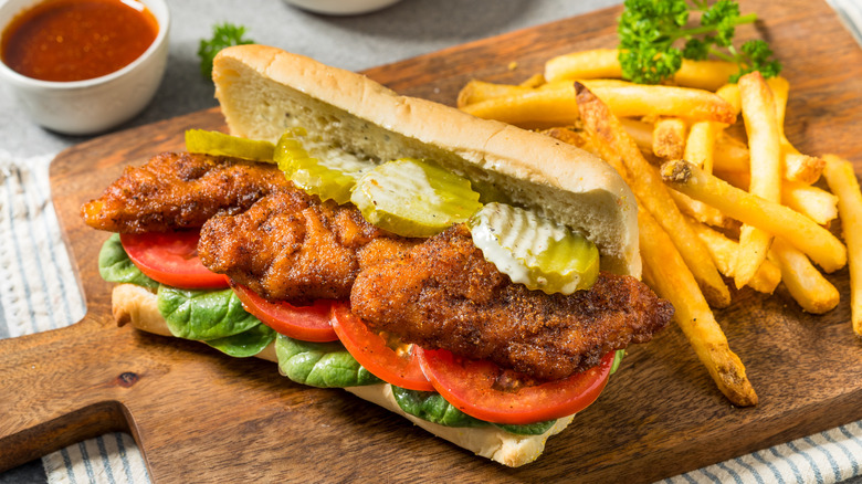 A fried fish sandwich is paired with fries on a cutting board.