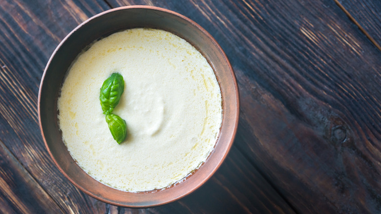 A ceramic bowl of Alfredo sauce on a wood surface