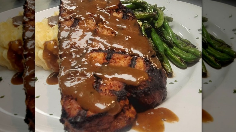 Close-up of grilled meatloaf with gravy, mashed potatoes, and green beans