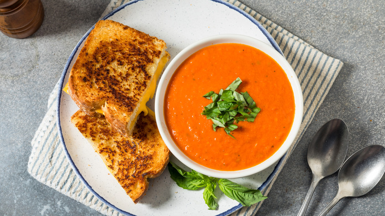 Tomato soup topped with basil in a white bowl and a grilled cheese sandwich cut in half on a blue-rimmed plate