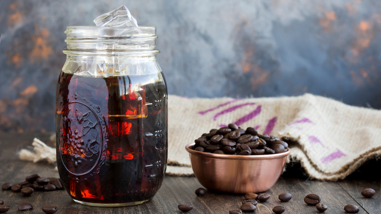 Mason jar with iced coffee next to coffee beans and burlap bag