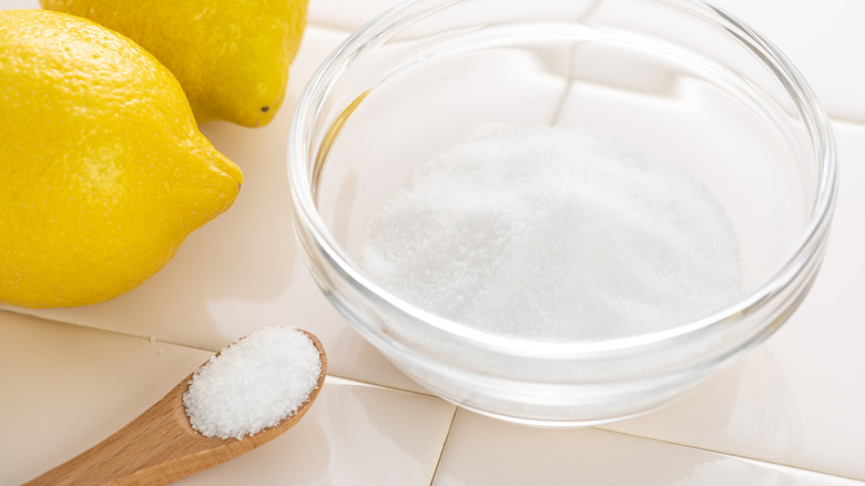 A bowl of citric acid sitting next to two lemons