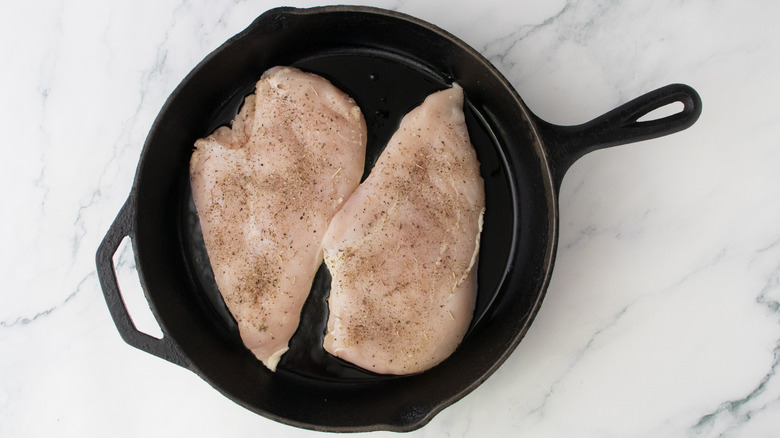 Two raw chicken cutlets cooking in a large skillet