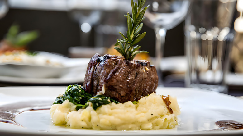 filet mignon steak plated atop mashed potatoes with a rosemary sprig garnish