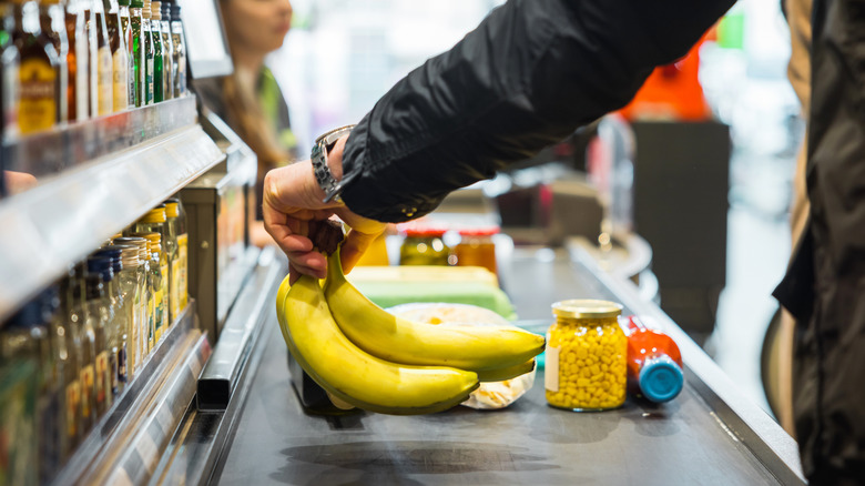 A person putting some bananas and other groceries on the conveyor at a store checkout.