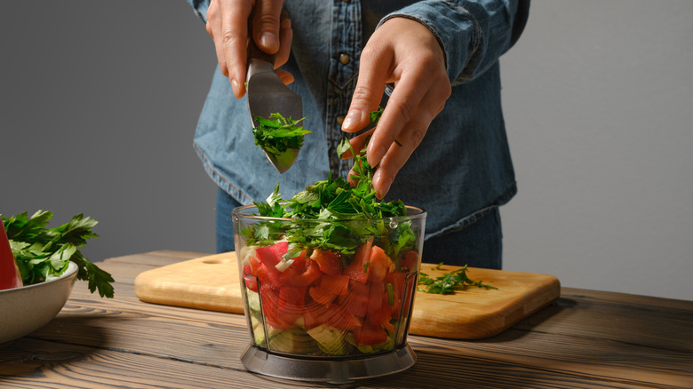 Person putting salsa ingredients into food processor