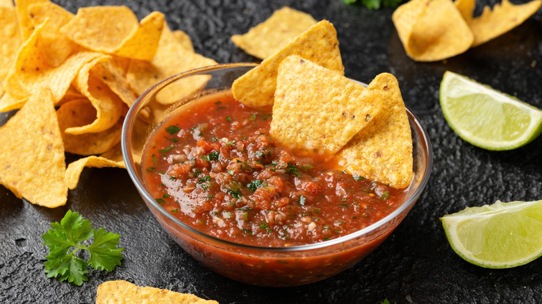 Clear bowl of salsa with tortilla chips and lime slices