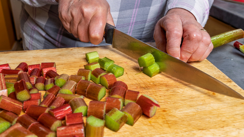 person chopping rhubarb with a knife and wooden cutting board