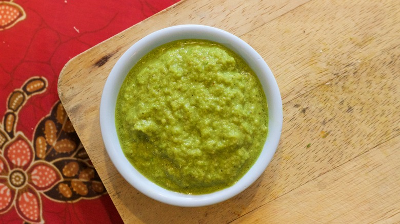 A small bowl of green curry paste on a wooden board