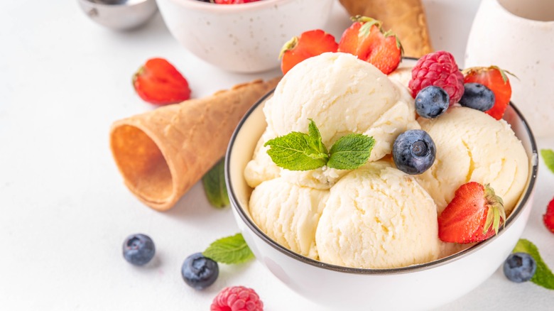 A bowl of white ice cream topped with berries and a sprig of mint