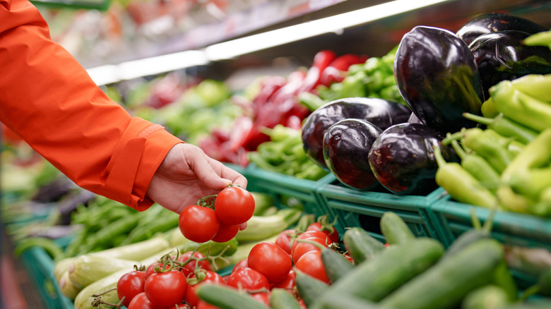 Hand selecting fresh tomatoes at grocery store.