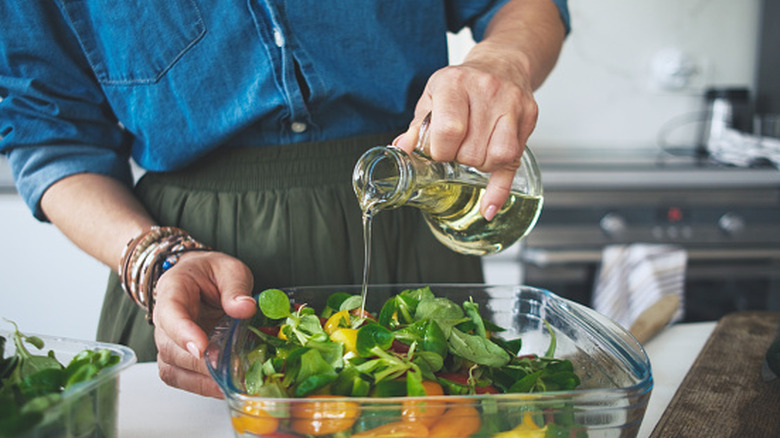 A woman adding olive oil in a salad.
