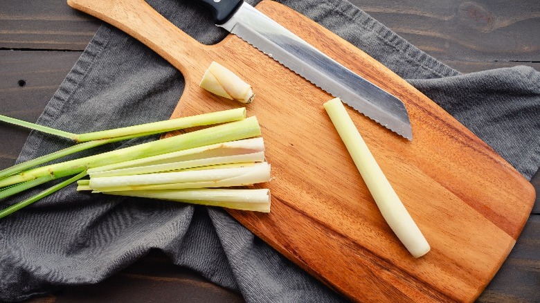 Cut lemongrass sits on a wooden cutting board with a knife