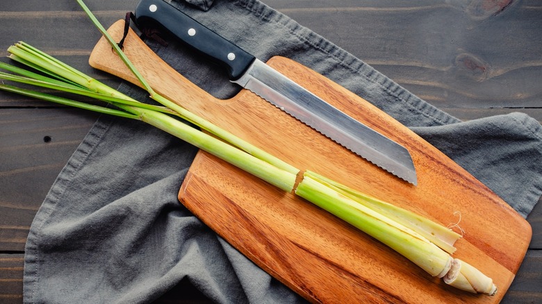 Fresh lemongrass sits on a wooden cutting board next to a knife