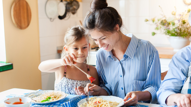 Mother and daughter eating pasta at home kitchen
