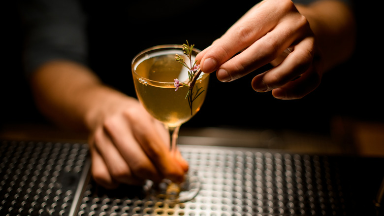 A bartender's hands garnishing a cocktail.