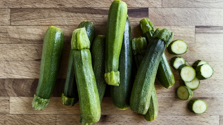 Several zucchinis and slices on wooden cutting board