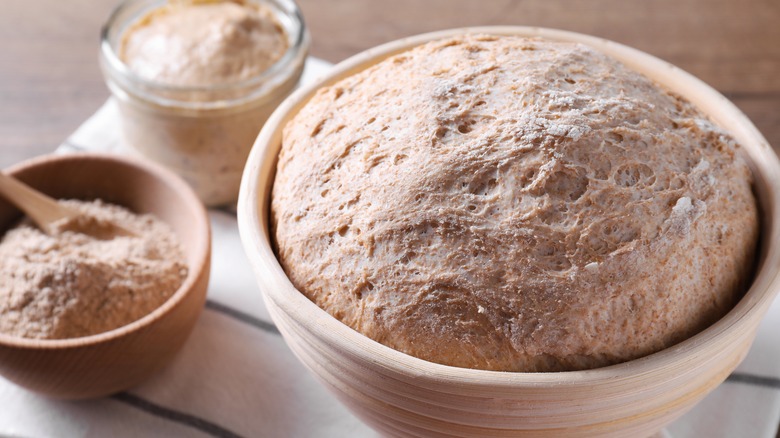 Close-up of sourdough in a proofing bowl surrounded by starter and flour