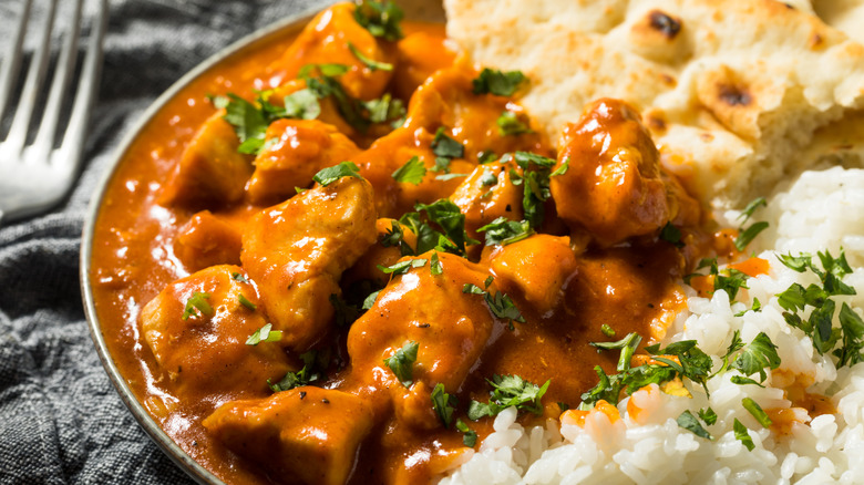 Plate full of rice, naan, and butter chicken sprinkled with cilantro