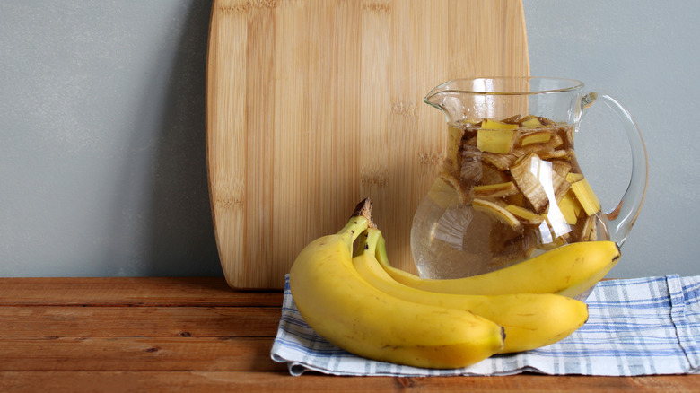 A glass pitcher of banana tea by a bamboo cutboard