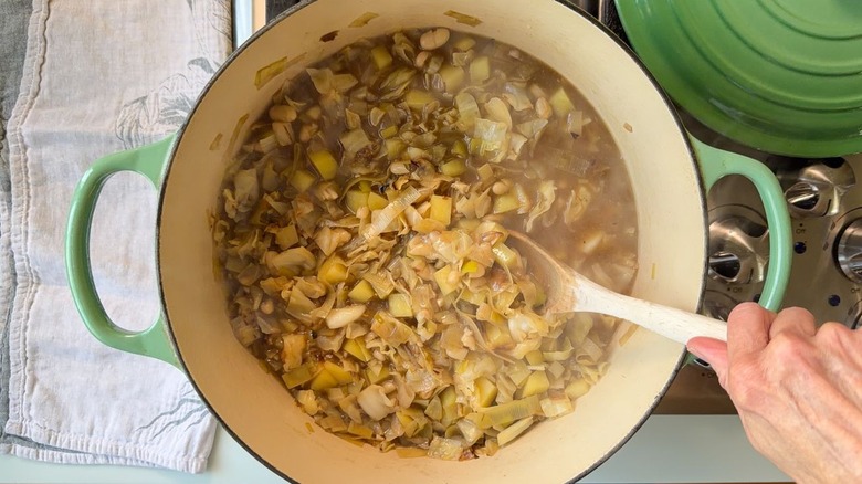 Stirring cabbage soup ingredients with wooden spoon in Dutch oven on stovetop