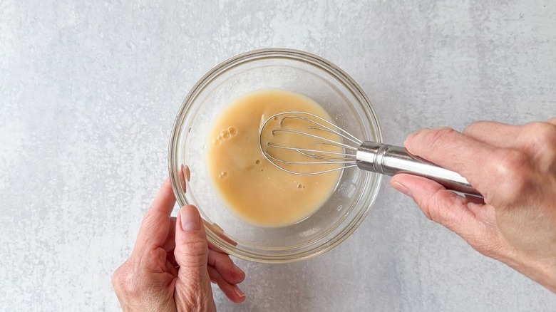 Whisking white miso paste with water in glass bowl