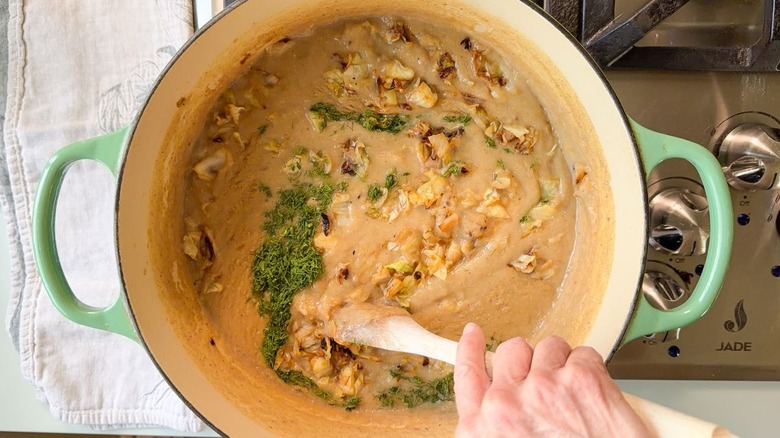 Stirring fresh dill and chopped charred cabbage into the cabbage soup in a Dutch oven