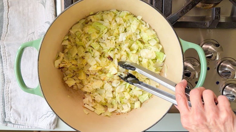 Turning charred green cabbage in Dutch oven on stovetop with tongs