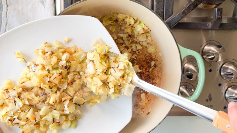 Transferring charred green cabbage from Dutch oven to plate with tongs