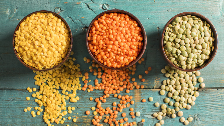 three colors of lentils in bowls on a green surface
