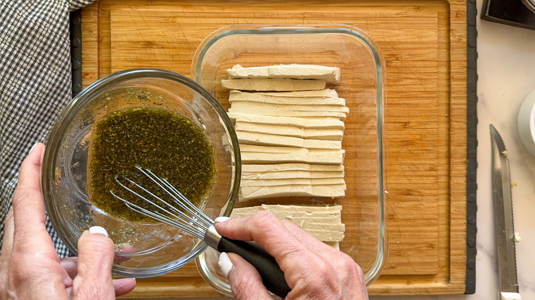 hand stirring marinade over tofu
