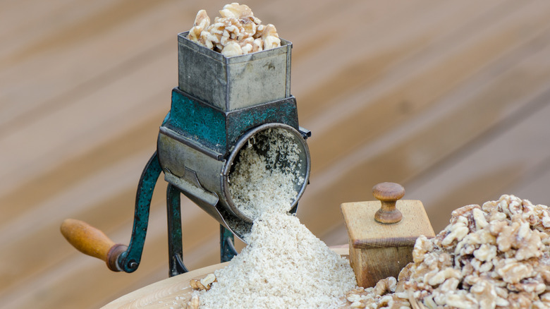 1930s hand-cranked steel nut grinder with a pile of walnuts and walnut flour.