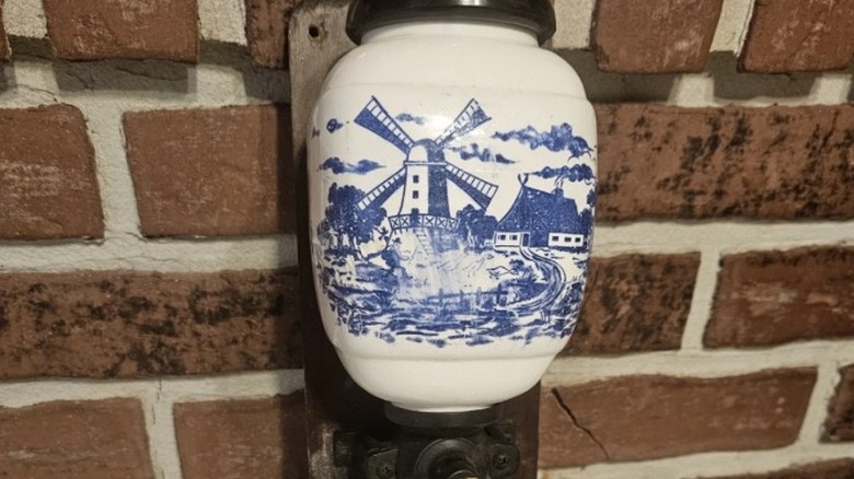 A Dutch Delft coffee mill with a blue and white design on a wood mount ready to be put on a wall.