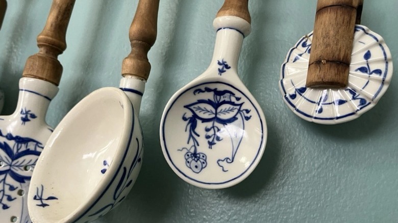A set of vintage German Meissen blue onion kitchen utensils with wooden handles hanging along a teal wall.