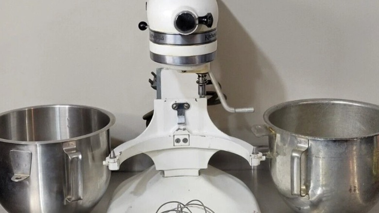A vintage Hobart era KitchenAid stand mixer with bowls on either side of it.