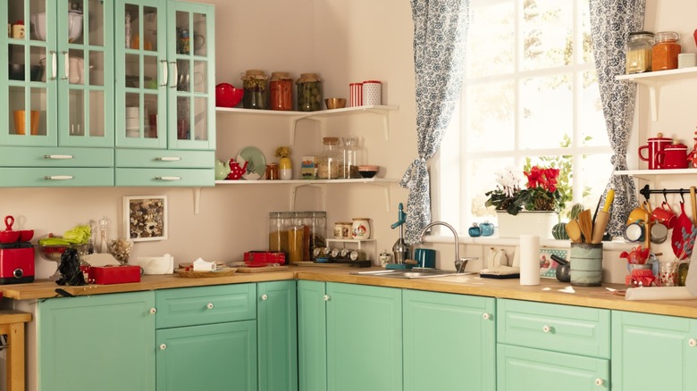 A retro kitchen with mint green cabinets and a lot of cooking tools and storage containers on shelves.