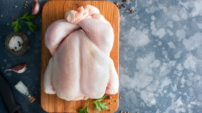 Whole raw chicken on a wooden board with spices for cooking, top view