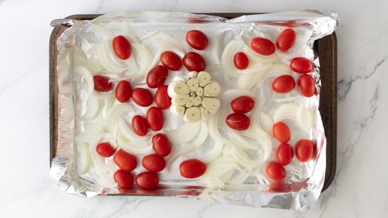 Cherry tomatoes, sliced onion, and garlic head on baking sheet