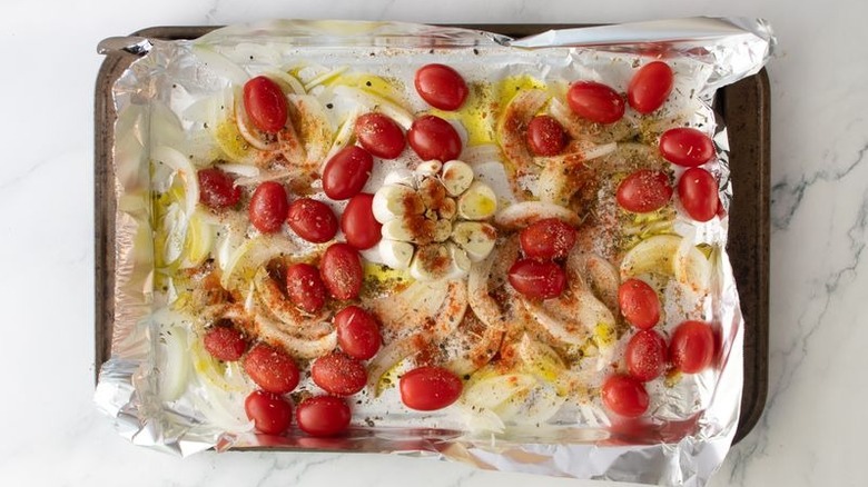 Tomatoes, onion, and garlic head drizzled with oil on baking sheet
